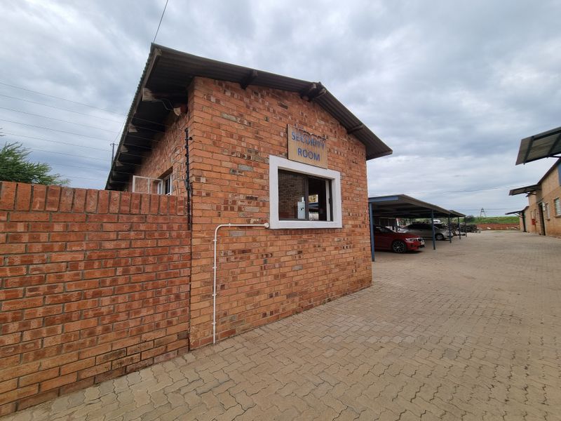 Exterior view of a commercial security room featuring face brick construction, paved driveway access, and adjacent covered parking structures.