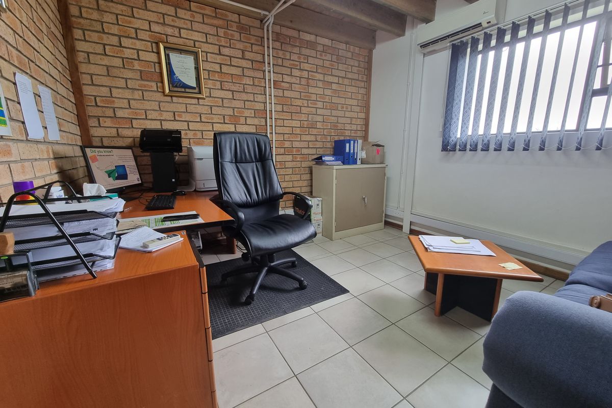 A functional commercial office space featuring exposed brick walls, timber ceiling beams, ceramic tiled flooring, and a wall-mounted air conditioning unit.