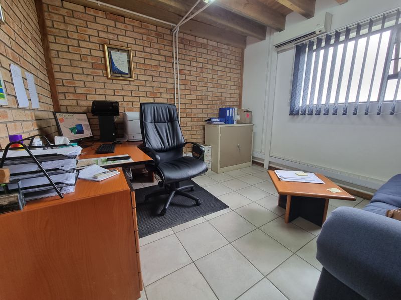 A functional commercial office space featuring exposed brick walls, timber ceiling beams, ceramic tiled flooring, and a wall-mounted air conditioning unit.