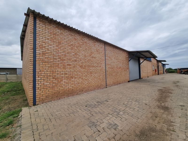 Exterior view of a commercial warehouse building featuring face brick walls, a corrugated metal roof, and a paved driveway with roller shutter access.