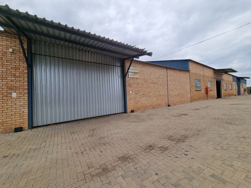 Commercial warehouse exterior featuring a large corrugated metal roller shutter door, face brick facade, and paved yard area for receiving and dispatch.