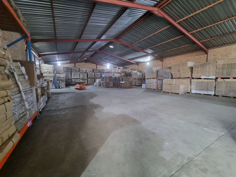 Spacious industrial warehouse featuring exposed steel roof trusses, durable concrete flooring, and face brick walls, suitable for storage or manufacturing operations.