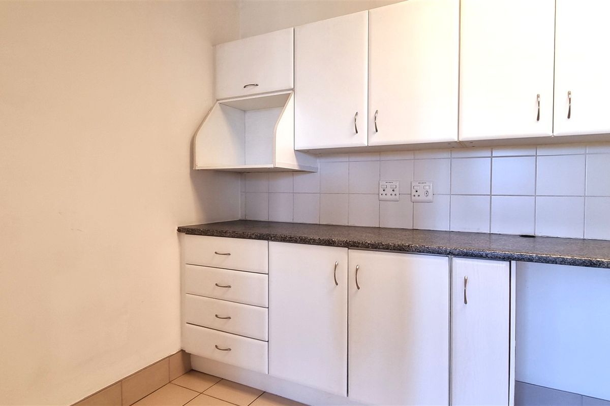 A functional kitchenette area featuring white cabinetry, dark laminate countertops, and tiled splashbacks, providing essential storage and workspace for an office environment.
