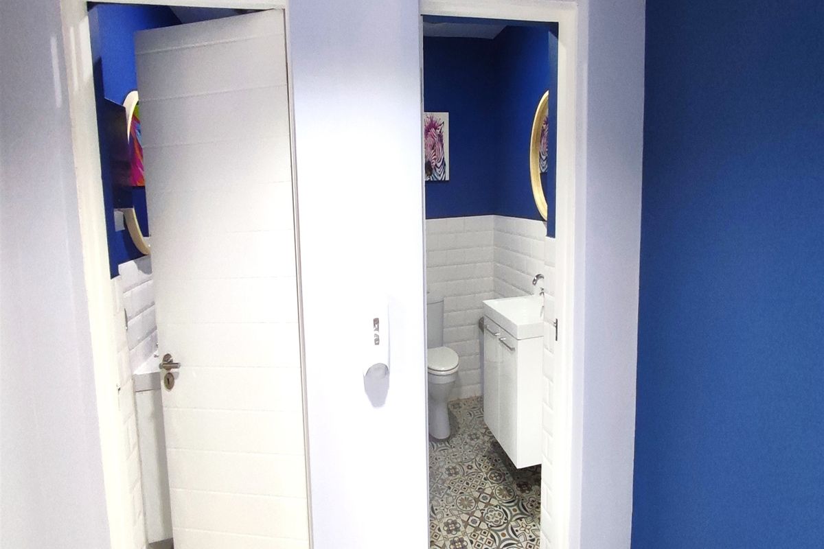 A view of two adjacent office restrooms featuring modern white vanity cabinets, subway tile backsplashes, and patterned floor tiling.