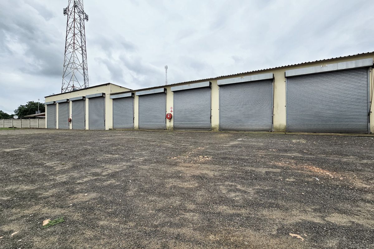 Industrial property featuring a row of multiple roller shutter doors and a large gravel yard area, suitable for storage or logistics operations.