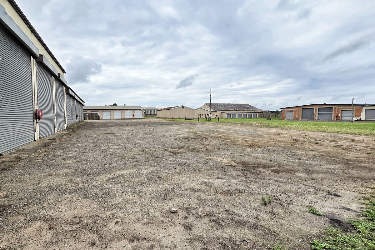 Expansive industrial yard featuring multiple warehouse units with roller shutter doors and a large unpaved gravel storage area.