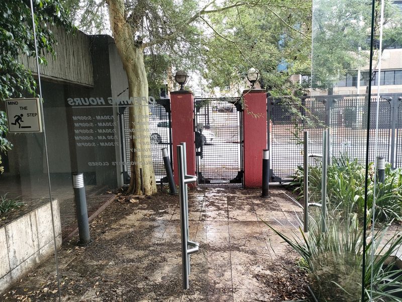 Entrance area featuring glass doors, paved walkway, and a secure metal gate with brick pillars, providing access to the industrial property.