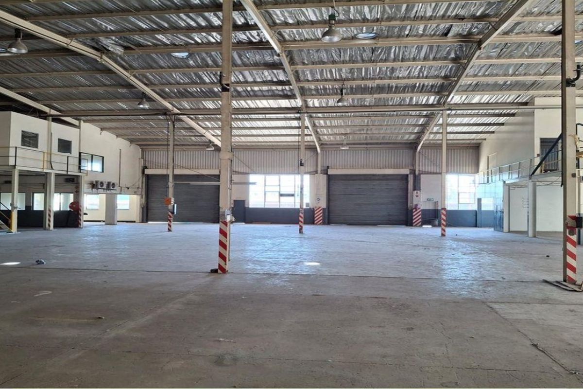 Spacious industrial warehouse featuring high ceilings, concrete flooring, multiple roller shutter doors, and a mezzanine level suitable for storage or manufacturing operations.