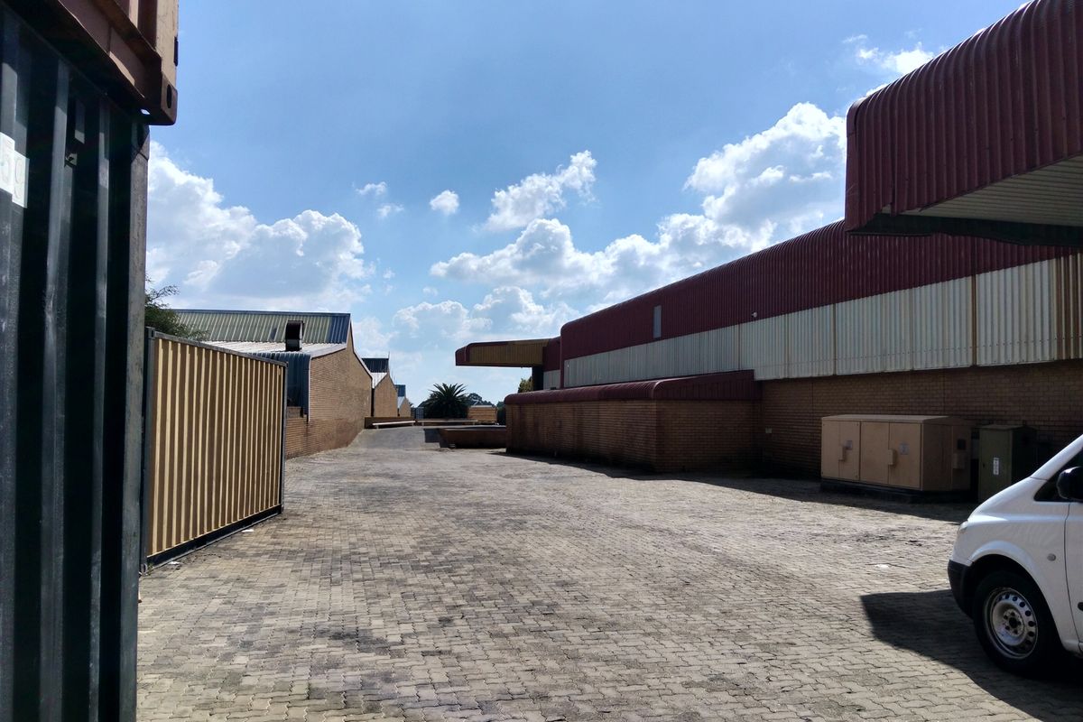 Exterior view of an industrial property featuring a paved yard area, brick warehouse walls, and metal roofing structures.