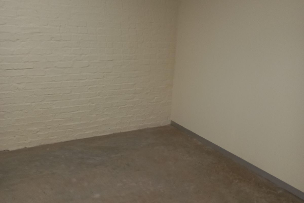An empty utility space featuring painted brick walls, concrete flooring, and exposed overhead mounting hardware.