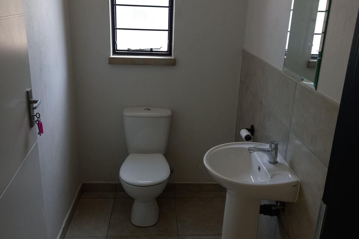 A functional guest bathroom featuring a pedestal basin, wall-mounted mirror, and a standard toilet with tiled flooring and splashback.