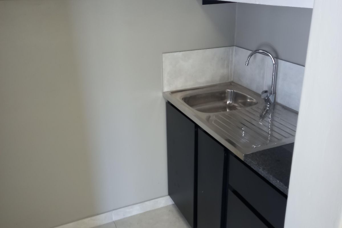 A compact scullery area featuring a stainless steel sink, modern dark cabinetry, tiled flooring, and a wall-mounted electrical distribution board.