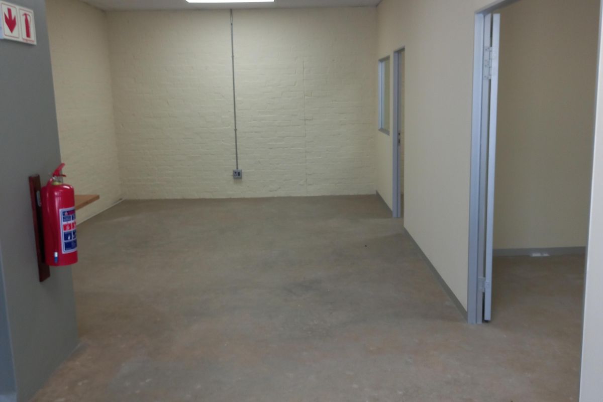 An empty commercial office space featuring a neutral color palette, recessed ceiling lighting, and exposed brick wall detailing.