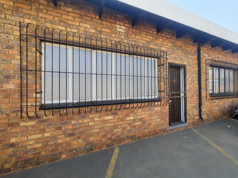 Exterior view of a commercial property featuring face brick facade, security bars on windows, and a secure entrance gate with asphalt parking area.