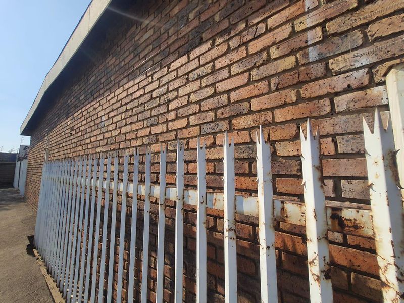Exterior view of a face brick wall secured with metal palisade fencing showing signs of surface corrosion.