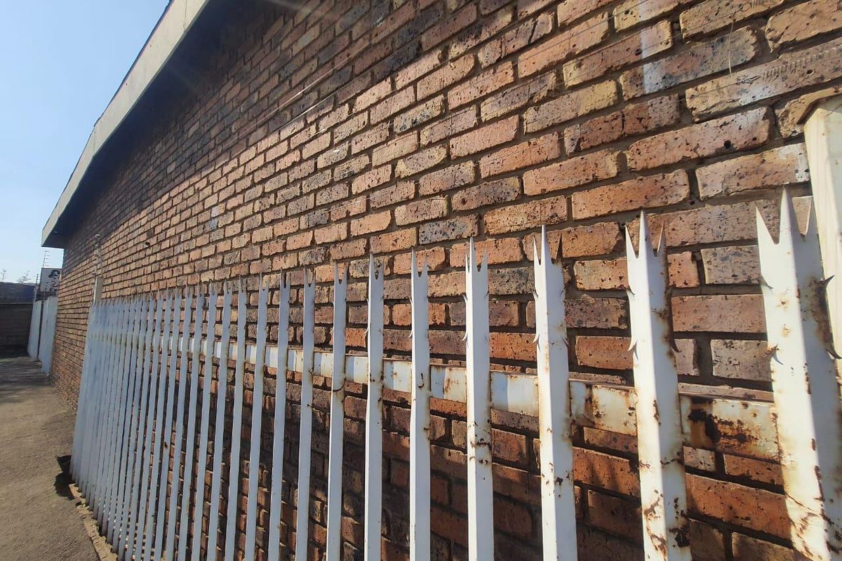 Exterior view of a face brick wall secured with metal palisade fencing showing signs of surface corrosion.