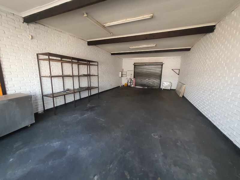 Spacious garage featuring painted brick walls, exposed timber ceiling beams, and a secure roller shutter door, suitable for storage or workshop use.
