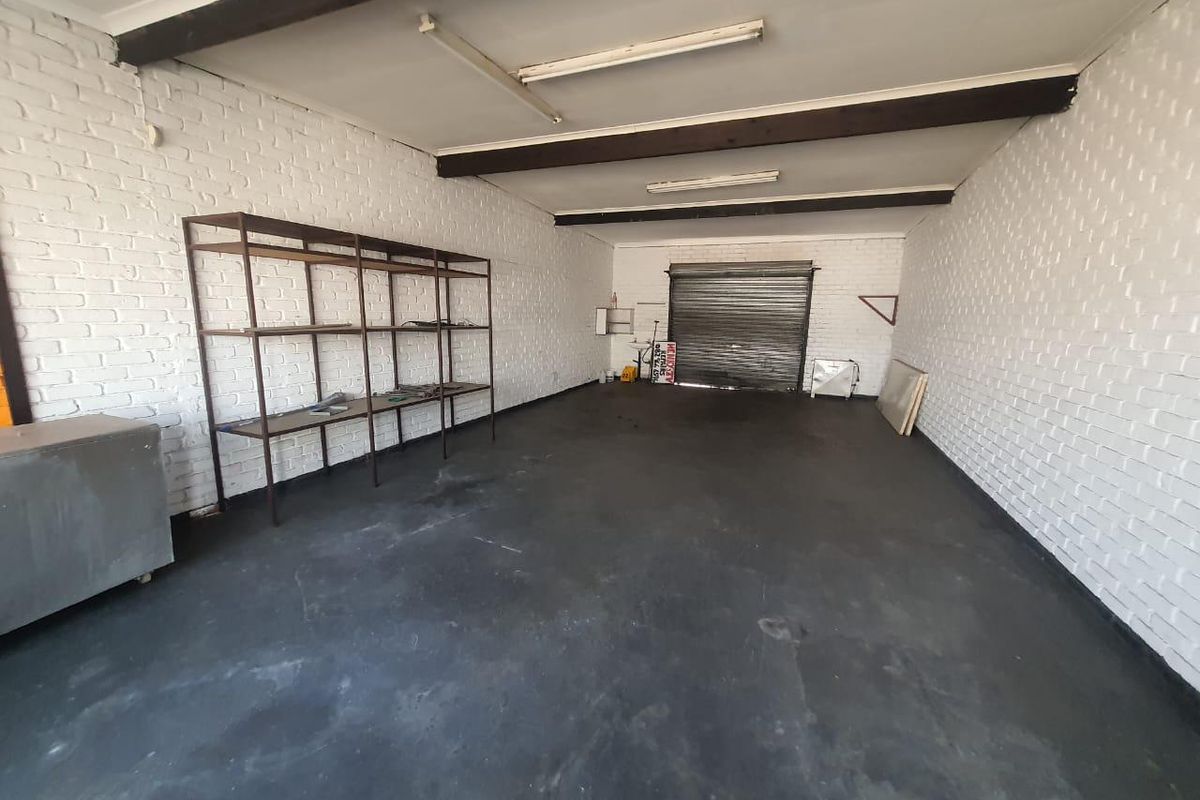 Spacious garage featuring painted brick walls, exposed timber ceiling beams, and a secure roller shutter door, suitable for storage or workshop use.