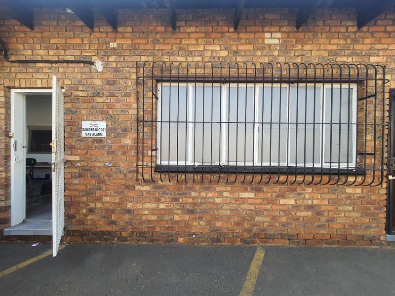 Exterior view of a commercial building featuring exposed brickwork, a window with security bars, and a metal security gate entrance.