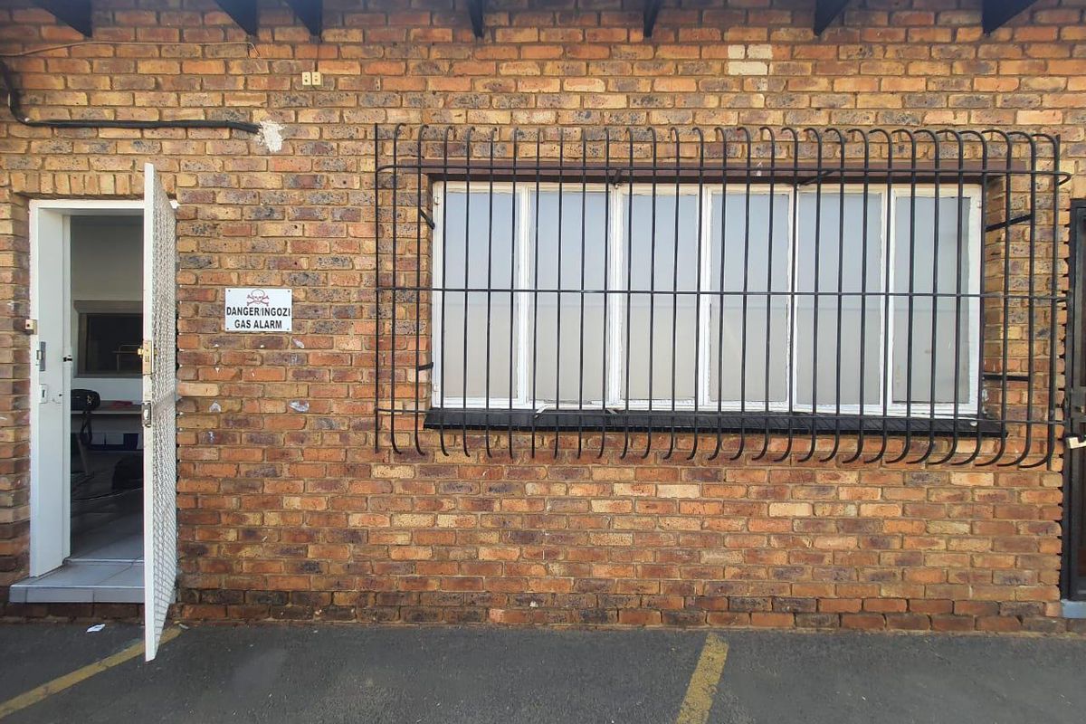 Exterior view of a commercial building featuring exposed brickwork, a window with security bars, and a metal security gate entrance.