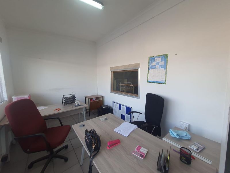 A functional office space featuring tiled flooring, fluorescent lighting, and an internal viewing window, suitable for a professional work environment.