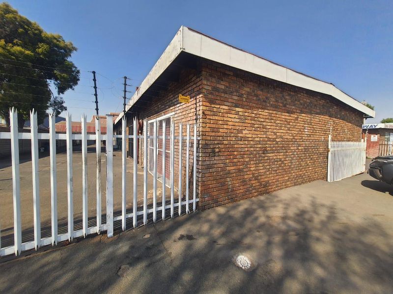 Exterior view of a face brick commercial building featuring secure perimeter fencing, electric security wires, and a paved driveway area.