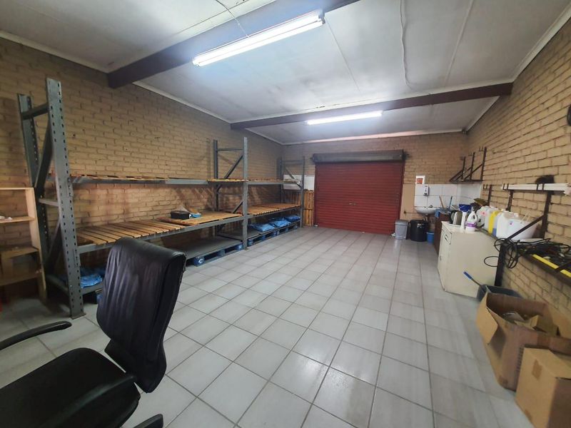 Spacious garage area featuring exposed brick walls, tiled flooring, fluorescent lighting, and a roller shutter door, suitable for storage or utility use.
