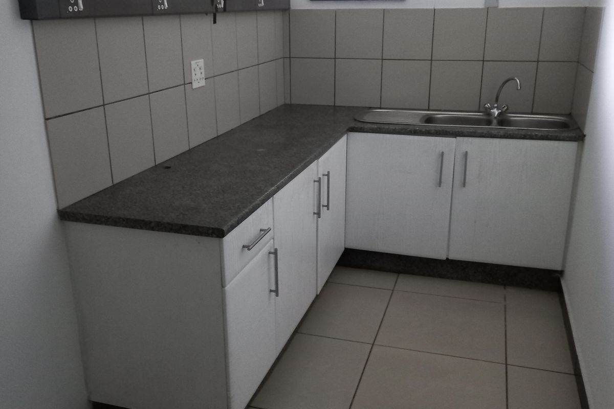 A functional kitchenette featuring white cabinetry, granite-look countertops, a stainless steel sink, and tiled flooring in a compact office space.