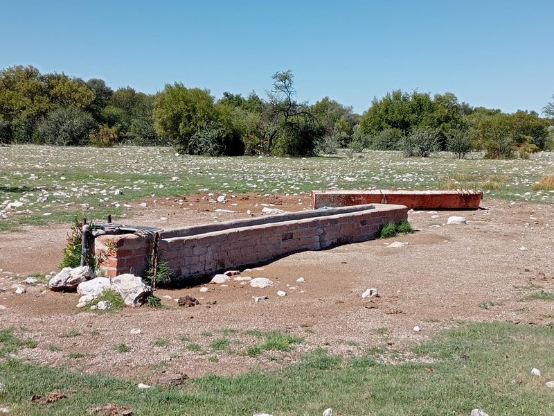 An outdoor livestock water trough constructed from brick, situated in an open farm field with surrounding natural landscape.