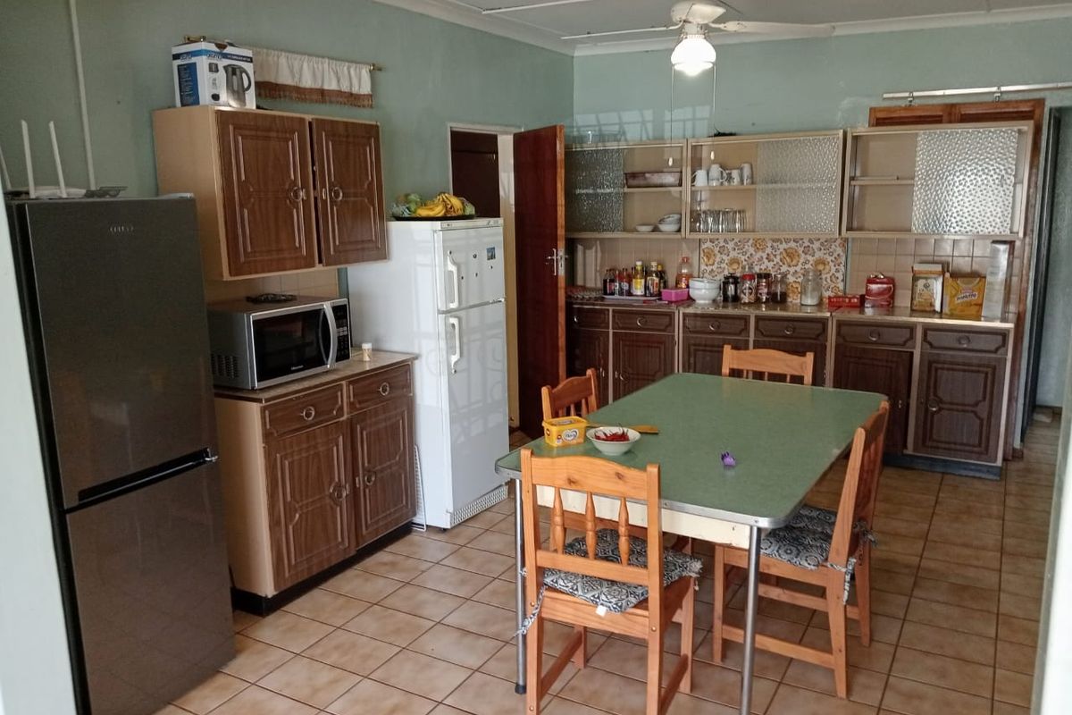 A functional kitchen featuring dated wooden cabinetry, tiled flooring, and a central ceiling fan, offering potential for modernization and aesthetic updates.