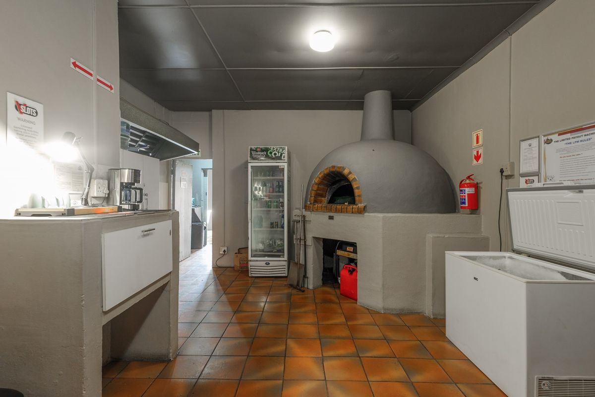 Commercial kitchen area featuring a built-in pizza oven, tiled flooring, and stainless steel extractor hood, suitable for food preparation and service.