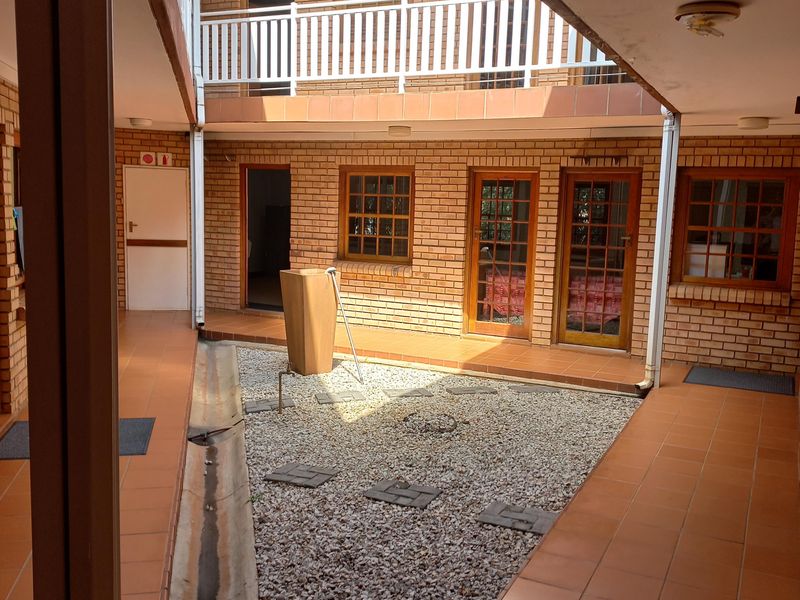A central brick-walled courtyard featuring a gravel garden, tiled walkways, and access to multiple office units via timber-framed doors and windows.