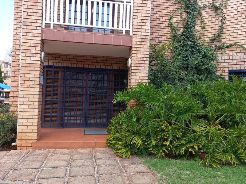 Front entrance of the office building featuring a brick facade, a covered balcony, and a secure gated entry with paved access.
