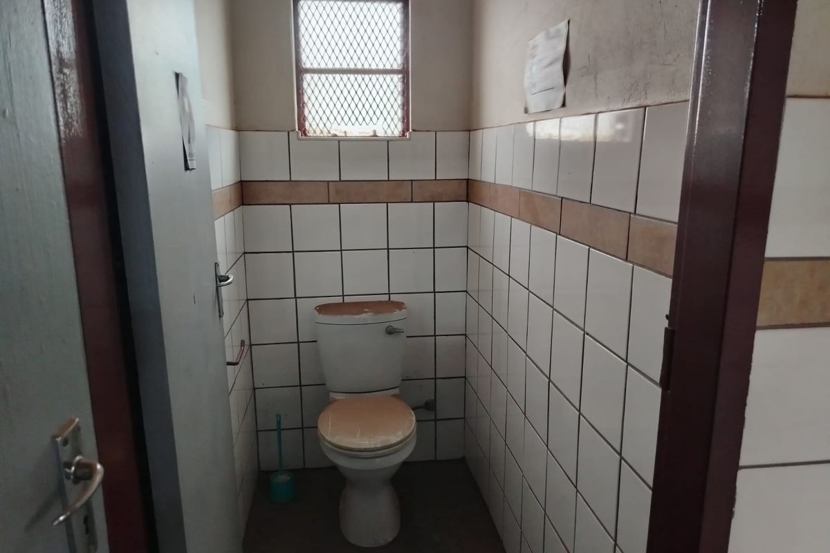 A small industrial bathroom featuring tiled walls, a standard toilet, and a security-grille window.
