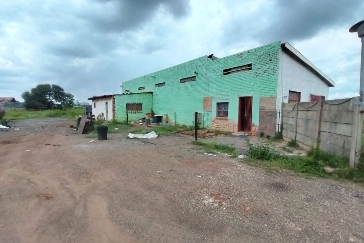 Rear view of an industrial building featuring painted brick walls, security gates, and a surrounding precast concrete boundary wall on a gravel lot.