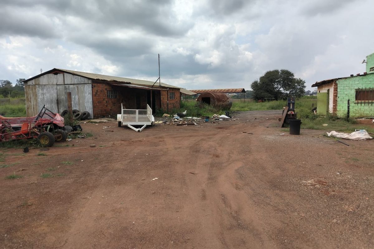 Industrial yard area featuring basic brick and corrugated metal structures with significant site maintenance required.