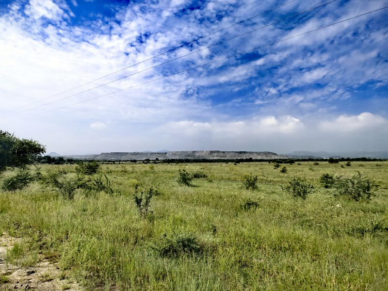 Expansive rural landscape view featuring open grassland and distant hills under a bright blue sky with overhead power lines.