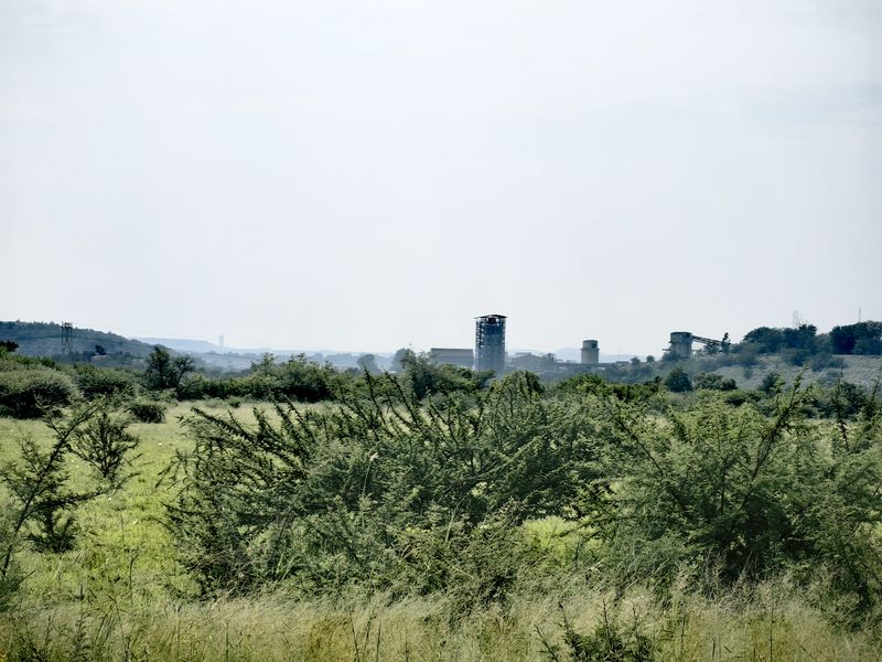 A scenic landscape view overlooking open fields with distant industrial structures and rolling hills in the background.