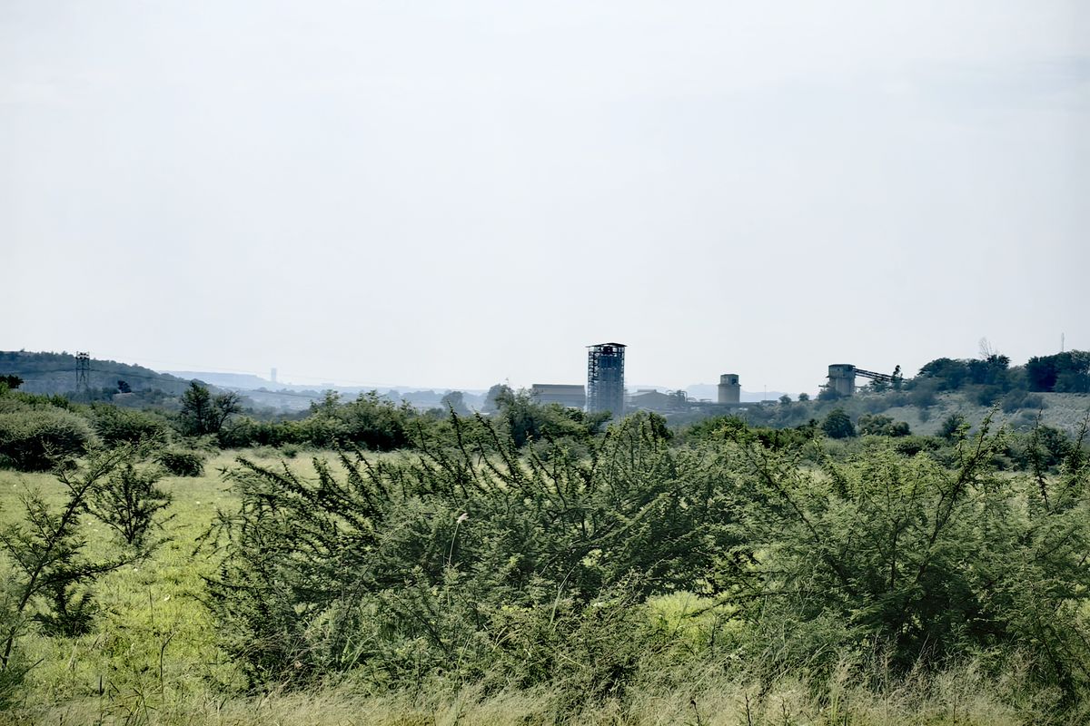 A scenic landscape view overlooking open fields with distant industrial structures and rolling hills in the background.