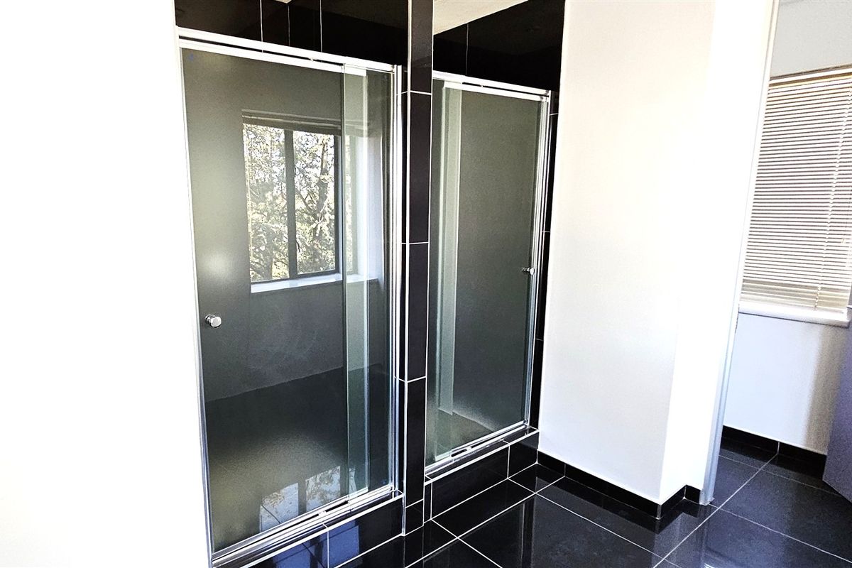 Modern office bathroom featuring dual glass-enclosed shower stalls, sleek black floor tiling, and high-contrast wall finishes.