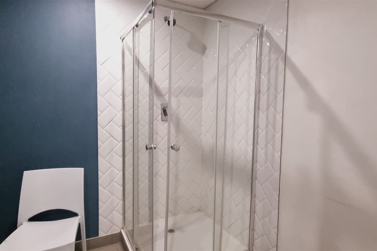 A modern bathroom featuring a glass-enclosed shower with white herringbone-patterned wall tiles and a contrasting dark blue accent wall.