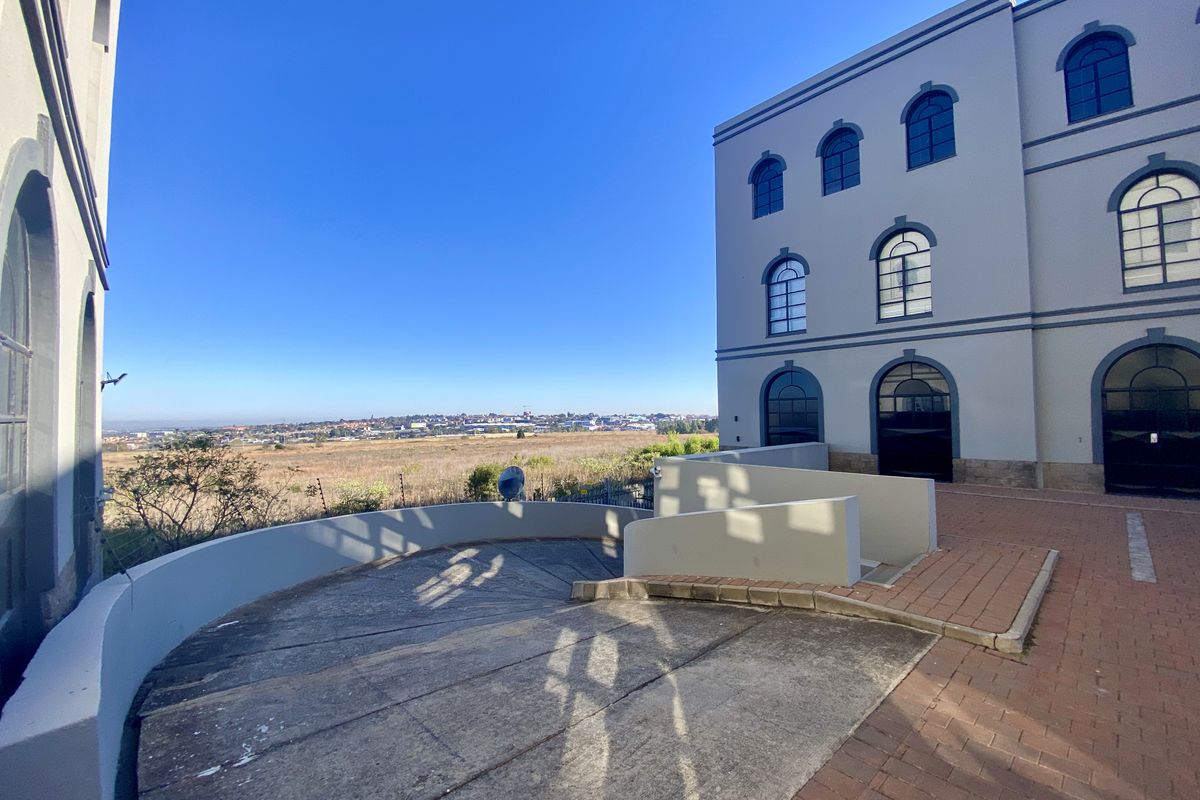 Exterior view of an industrial building featuring a concrete ramp, paved driveway, and arched windows overlooking an open landscape.