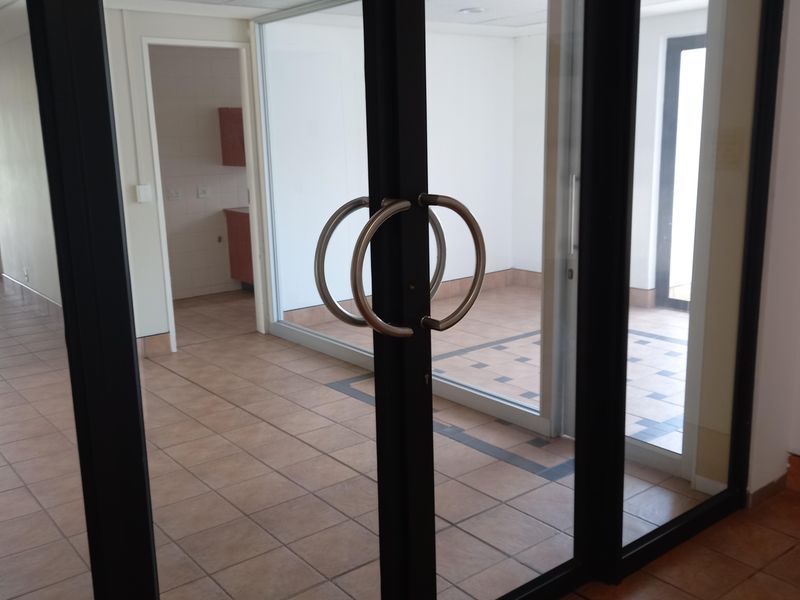 Empty office space featuring glass partitions with black aluminium frames, ceramic tiled flooring, and a suspended ceiling with recessed lighting.