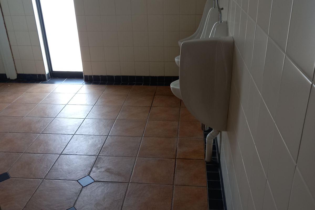 A functional office restroom featuring wall-mounted urinals, tiled walls, and durable ceramic floor tiles.