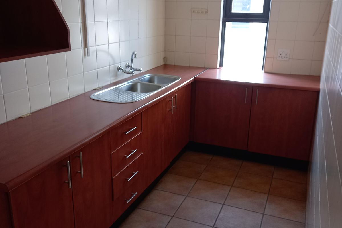 A functional office kitchenette featuring laminate countertops, built-in wooden cabinetry, a stainless steel double sink, and tiled flooring.