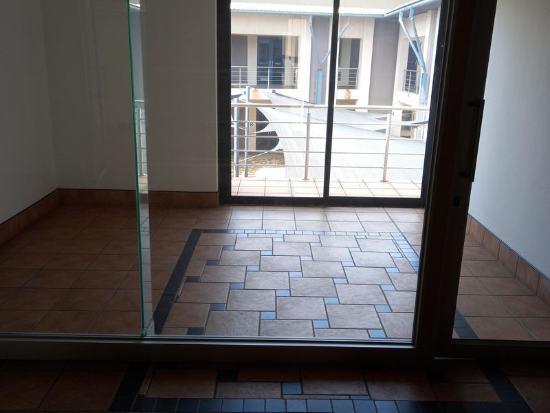 An empty office space featuring tiled flooring, a glass partition, and a sliding door leading to an outdoor balcony area.