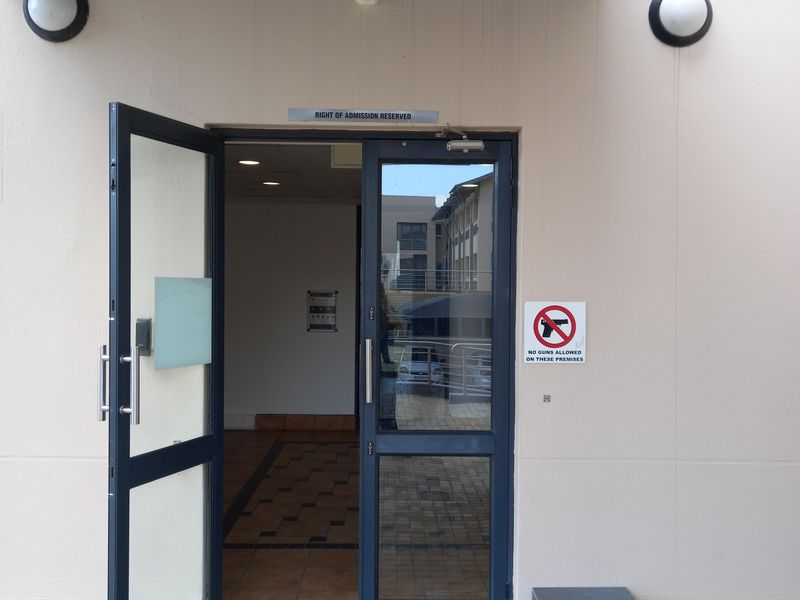 Office building entrance featuring a glass and metal door, security camera, and external lighting under a metal awning.