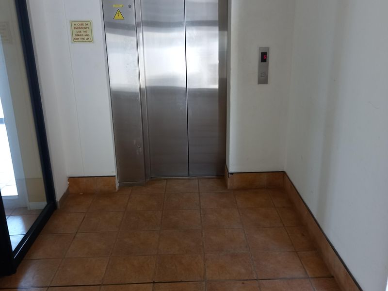 A clean office building hallway featuring a stainless steel elevator and durable ceramic floor tiling.