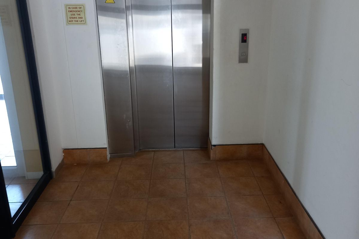 A clean office building hallway featuring a stainless steel elevator and durable ceramic floor tiling.
