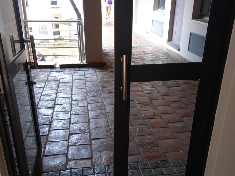 A view through an open glass door into a tiled outdoor corridor or walkway area with metal railings.